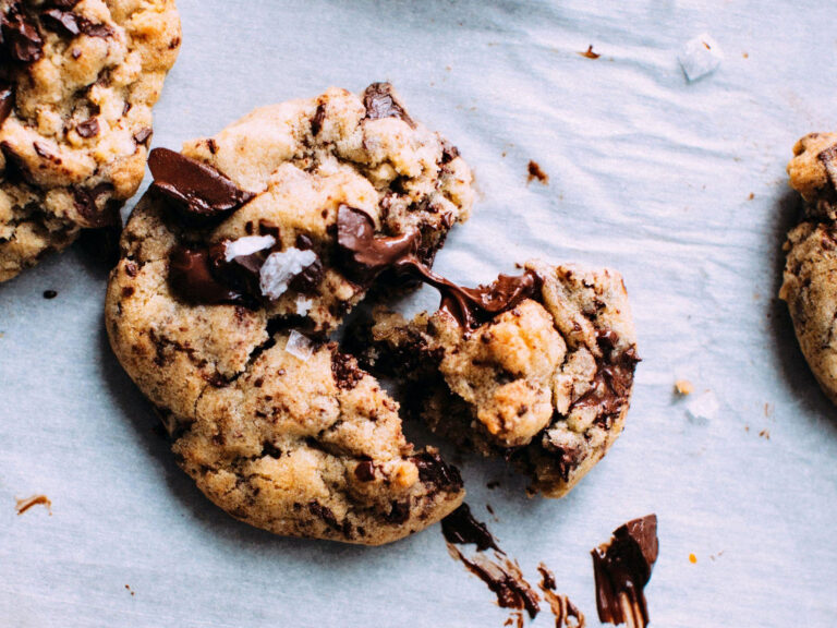 Close-up of a freshly baked chocolate chip cookie being split in half, revealing a soft, gooey center with melted chocolate chips
