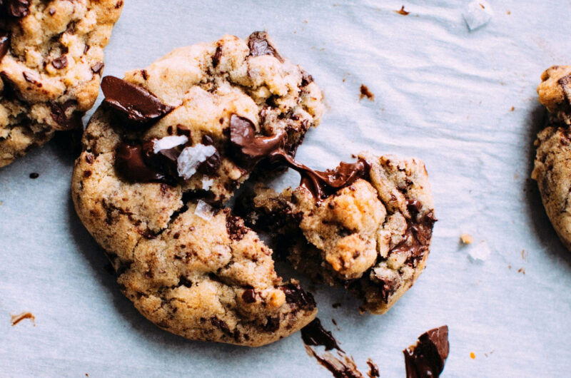 Close-up of a freshly baked chocolate chip cookie being split in half, revealing a soft, gooey center with melted chocolate chips