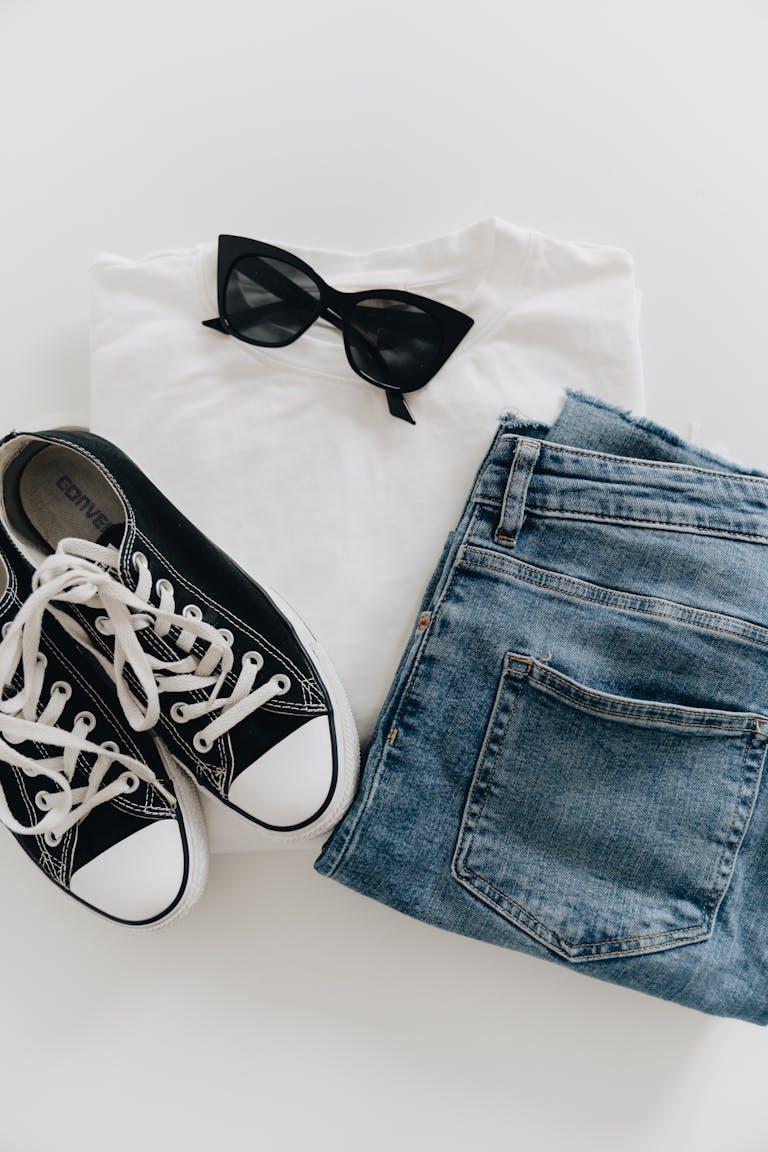 Flat lay of jeans, sneakers, and sunglasses for a modern casual style.
