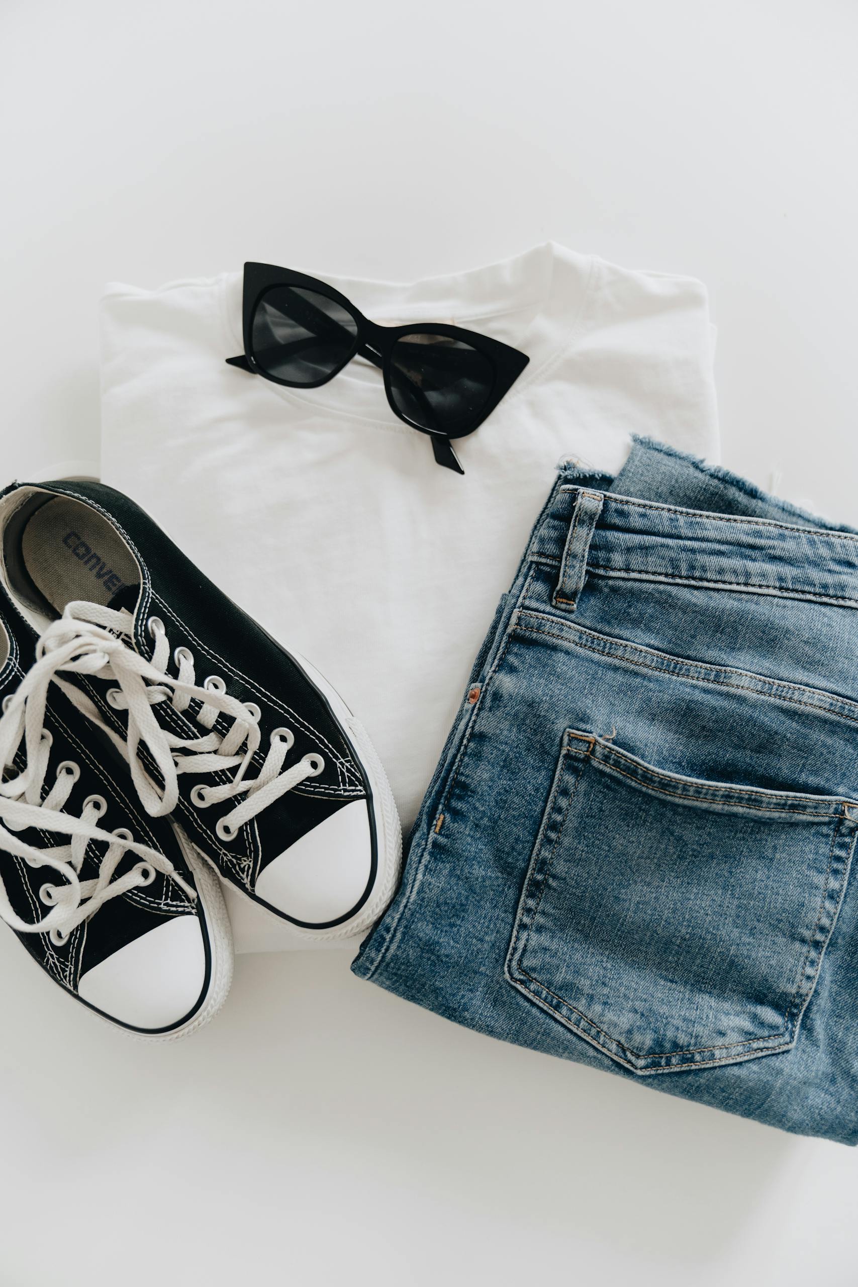 Flat lay of jeans, sneakers, and sunglasses for a modern casual style.
